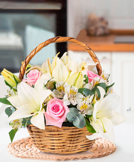 Cesta de mimbre con lirios blancos, rosas rosadas, hojas verdes y alstroemeria blanca