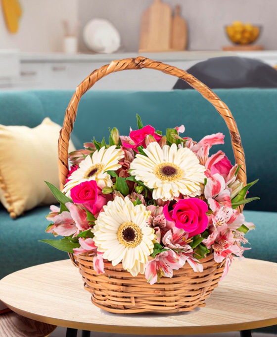 Cesta de mimbre con gerberas amarillentas, rosas fucsias y alstroemerias rosadas